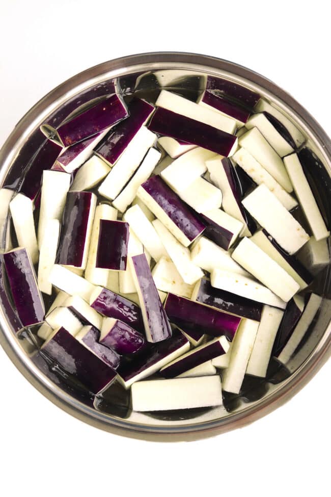 Eggplant strips soaking in bowl filled with lightly salted water.