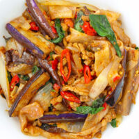 Closeup of plate with stir-fried rice noodles, pork, eggplant, chilies and basil.