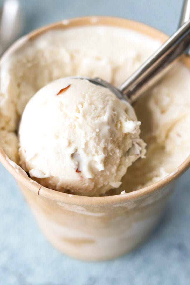 Scoop of amaretto ice cream in an ice cream scooper inside a pint with ice cream.