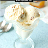 Ice cream scoops in a dessert glass and spoons on the side. Text overlay "No Churn Amaretto Ice Cream with Honey Roasted Almonds" and "thatspicychick.com".