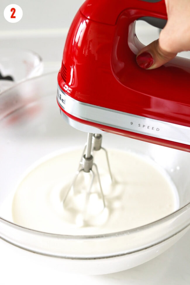 Hand using an electric hand mixer to beat cream in a large mixing bowl.