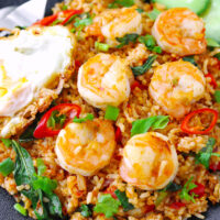 Black plate with spicy shrimp fried rice and a fried egg. Text overlay "Thai Red Curry Fried Rice with Shrimp & Thai Style Fried Egg" and "thatspicychick.com".