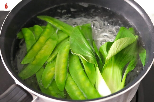 Cooking noodles and blanching bok choy and snow peas in a pot.