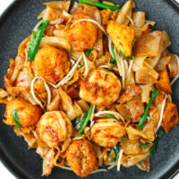 Char Kway Teow with shrimp, fried tofu puffs, and bean sprouts on a black plate.