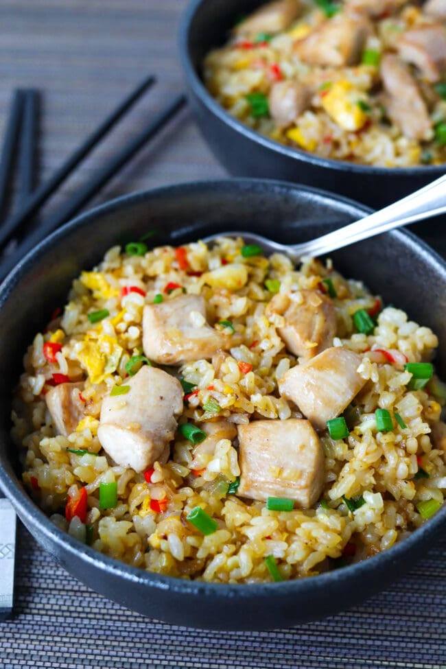 Closeup of two bowls with chicken and egg fried rice and a spoon.