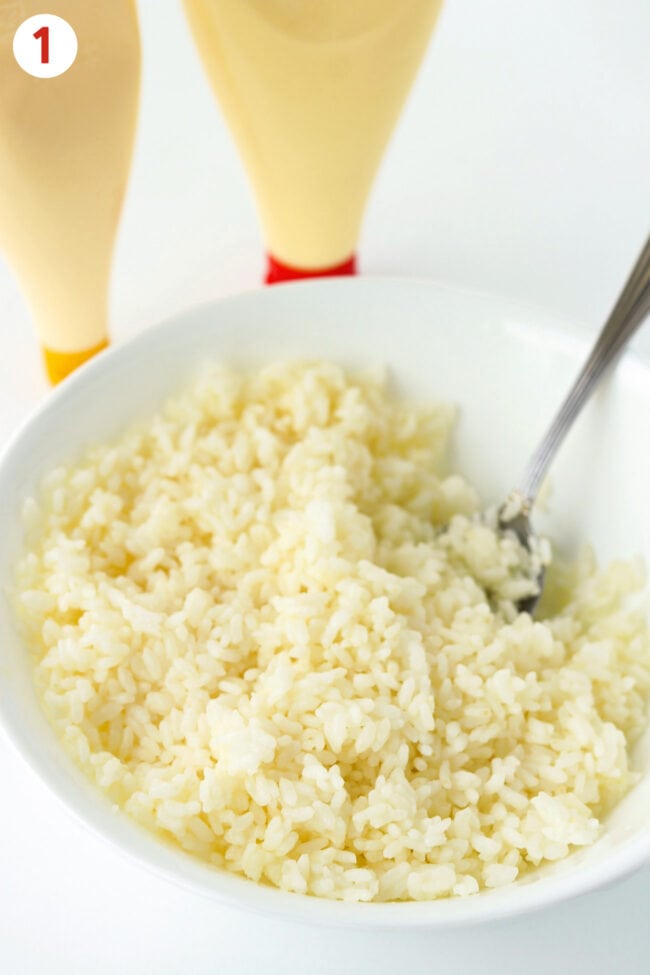 Bowl of rice mixed with mayonnaise. Kewpie mayonnaise and mustard mayonnaise squeezable bottles behind.