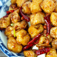 Closeup of tofu stir-fry on a plate. Text overlay "Kung Pao Tofu Puffs" and "thatspicychick.com".