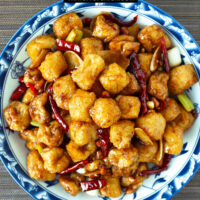 Plate with spicy tofu stir-fry. Text overlay "Kung Pao Tofu Puffs" and "thatspicychick.com".