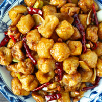 Closeup of plate with kung pao tofu stir-fry. Text overlay "Kung Pao Tofu Puffs" and "thatspicychick.com".