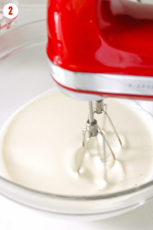 Beating heavy whipping cream with an electric hand mixer in a mixing bowl.