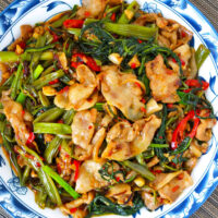 Closeup top view of plate with pork and vegetables stir-fry. Text overlay "XO Sauce Pork and Water Spinach Stir-fry" and "thatspicychick.com".