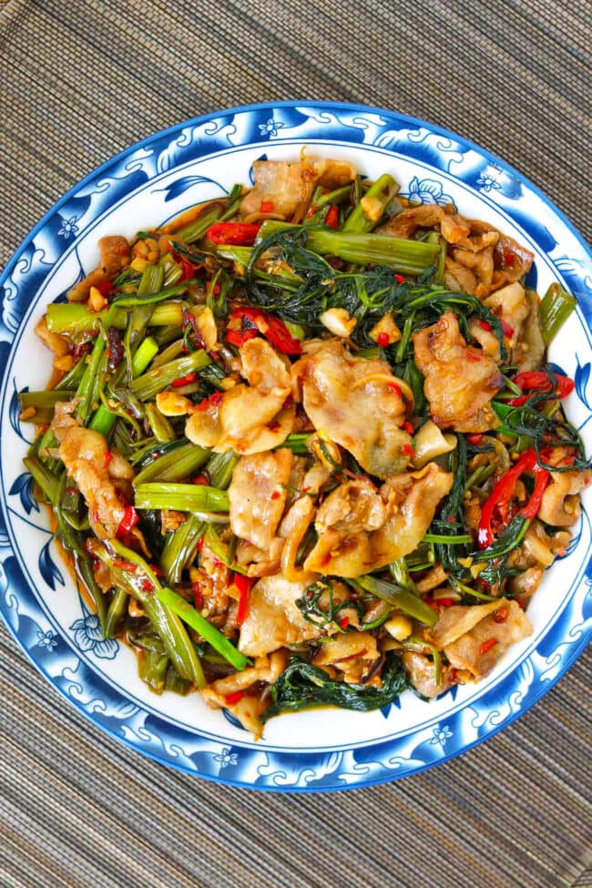 Plate with thin sliced pork belly and water spinach stir-fry.