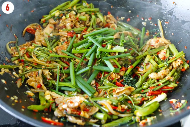 Added spring onion to pork and water spinach stir-fry in a wok.
