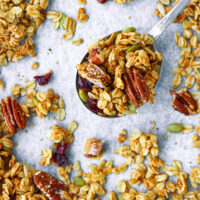 Granola on a big spoon on a baking tray with granola. Text overlay "High Protein Granola", "Easy | Healthy | GF | DF", and "thatspicychick.com".