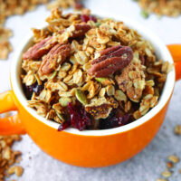 Closeup of granola in a bowl with handles. Text overlay "High Protein Granola", "Easy | Vegan | GF | DF", and "thatspicychick.com".
