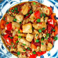 Closeup of plate with chicken and red bell pepper stir-fry. Text overlay "Sichuan Garlic Chicken Stir-fry" and "thatspicychick.com".