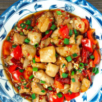 Plate with chicken and red bell pepper stir-fry. Text overlay "Sichuan Garlic Chicken Stir-fry" and "thatspicychick.com".