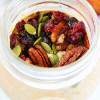 Closeup of pumpkin overnight oats in a jar topped with pecans, cranberries, and pumpkin seeds.