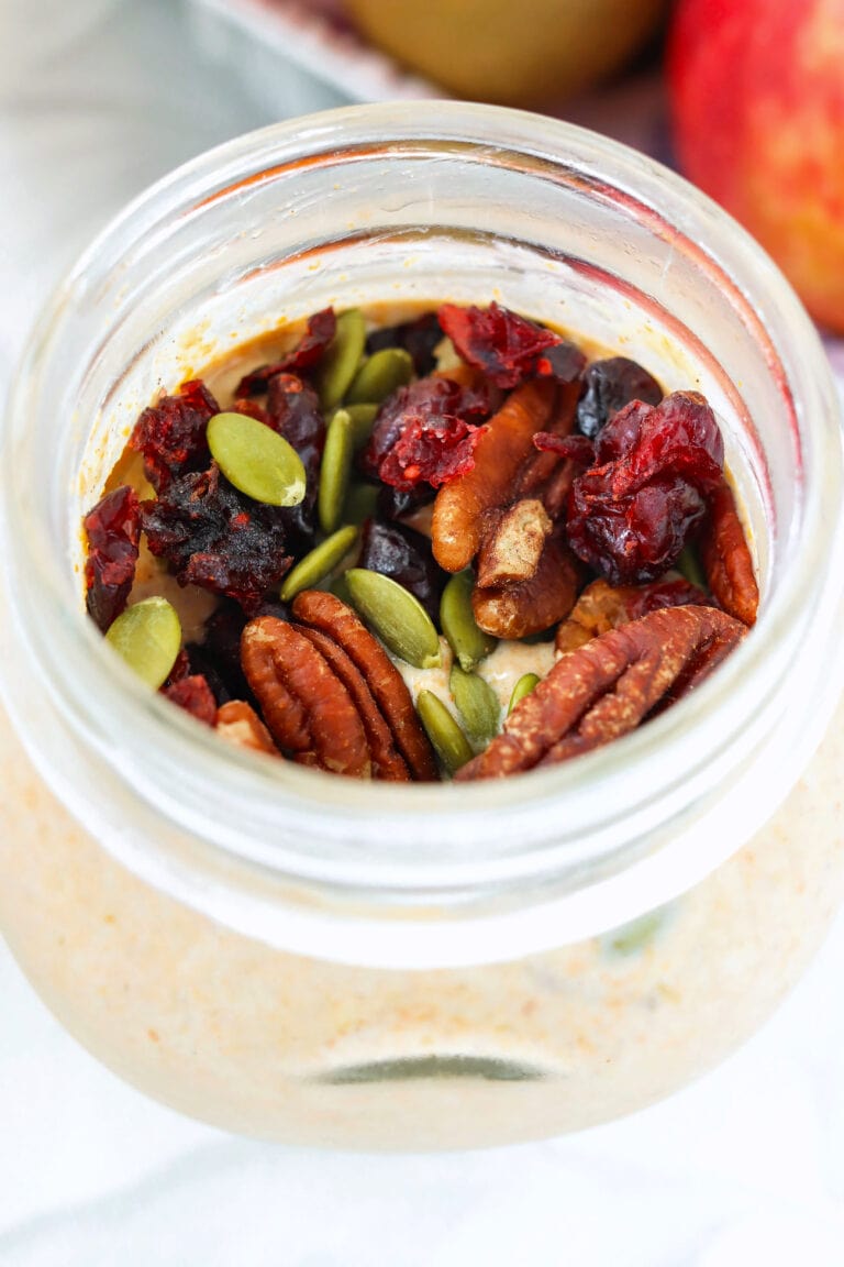 Pumpkin spice overnight oats topped with pumpkin seeds, pecans and dried cranberries in a small jar.