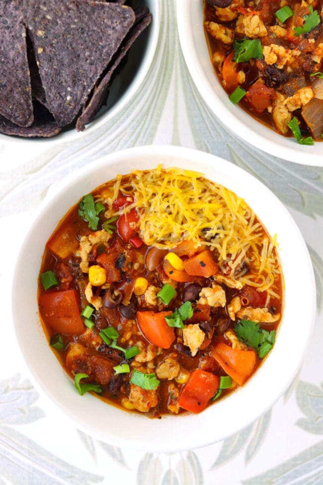 Two bowls with ground chicken chili and a bowl with tortilla chips.