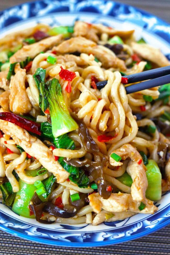 Chopsticks noodle pull from plate with a spicy stir-fried chicken noodles dish.