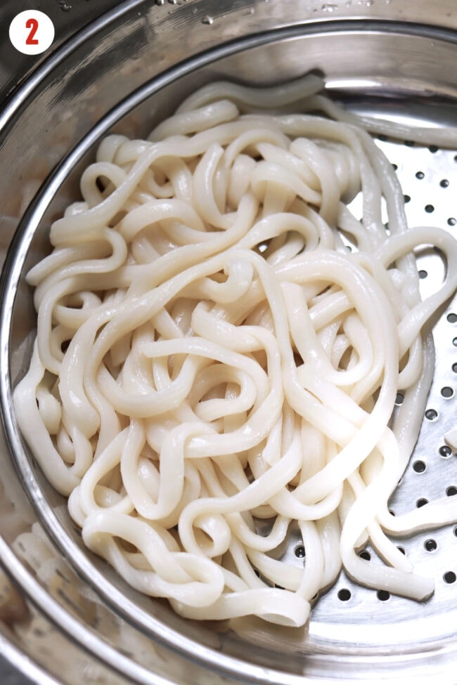 Cooked udon noodles in a colander.
