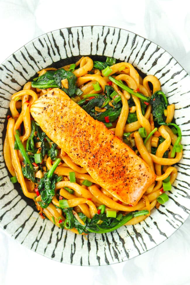 Pan-fried salmon on stir-fried spicy cumin noodles on a plate.