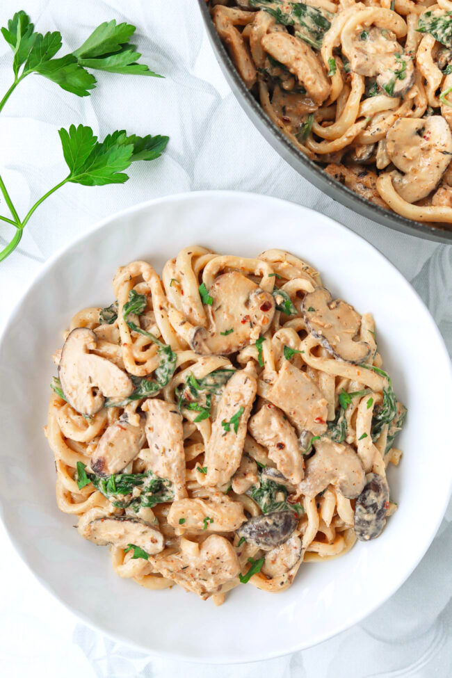 Plate and pan with Creamy Mushroom Udon with Chicken topped with chopped parsley.