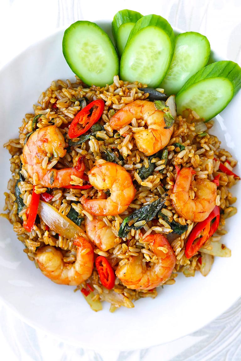 Closeup top view of Thai holy basil shrimp fried rice on a plate with sliced cucumber.