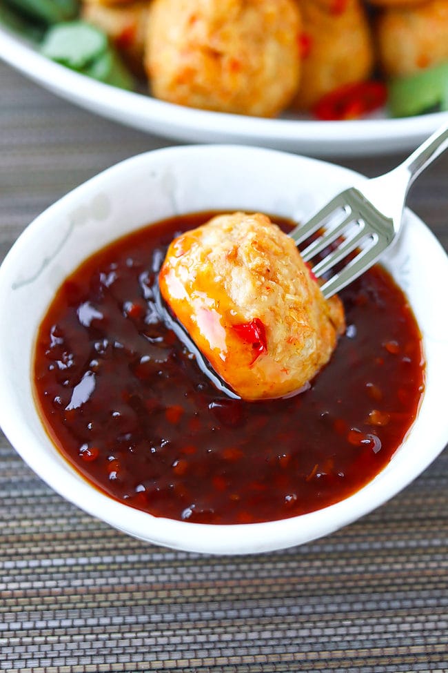 Chicken meatball pierced with a fork in a bowl of Thai sweet chili sauce.