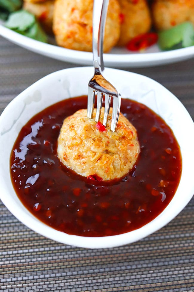 Thai chicken meatball pierced with a fork in a bowl of Thai sweet chili sauce.