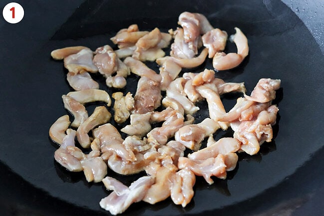 Cooking marinated chicken thigh pieces in a large wok.