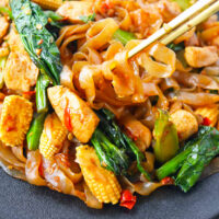 Chopsticks digging into a plate with stir-fried noodles with chicken. Text overlay "Shirataki Drunken Noodles" and "thatspicychick.com".