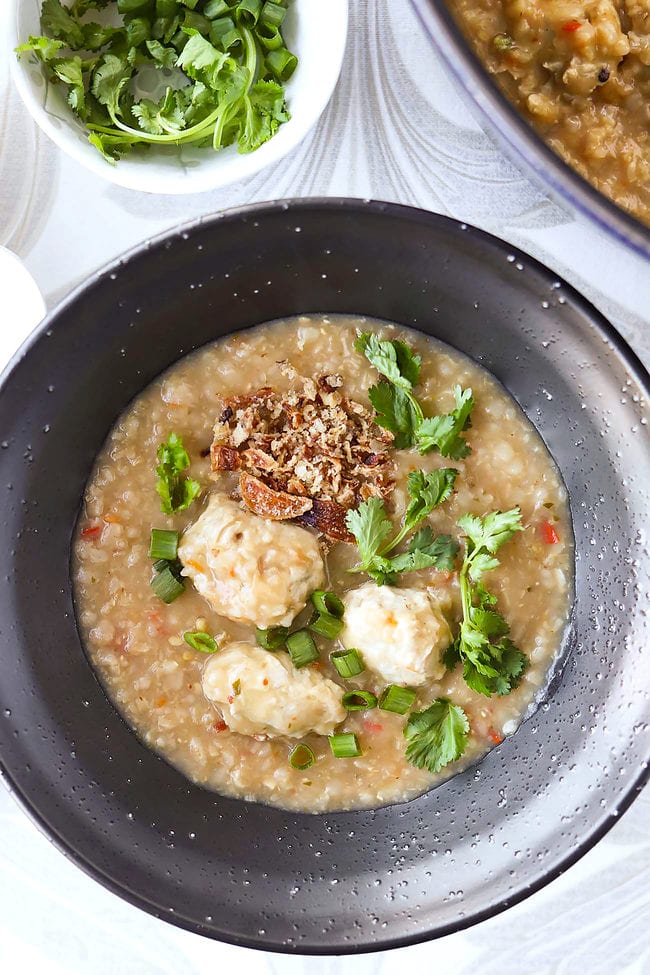 Thai congee with chicken meatballs topped with coriander, spring onion and fried shallots in a bowl.