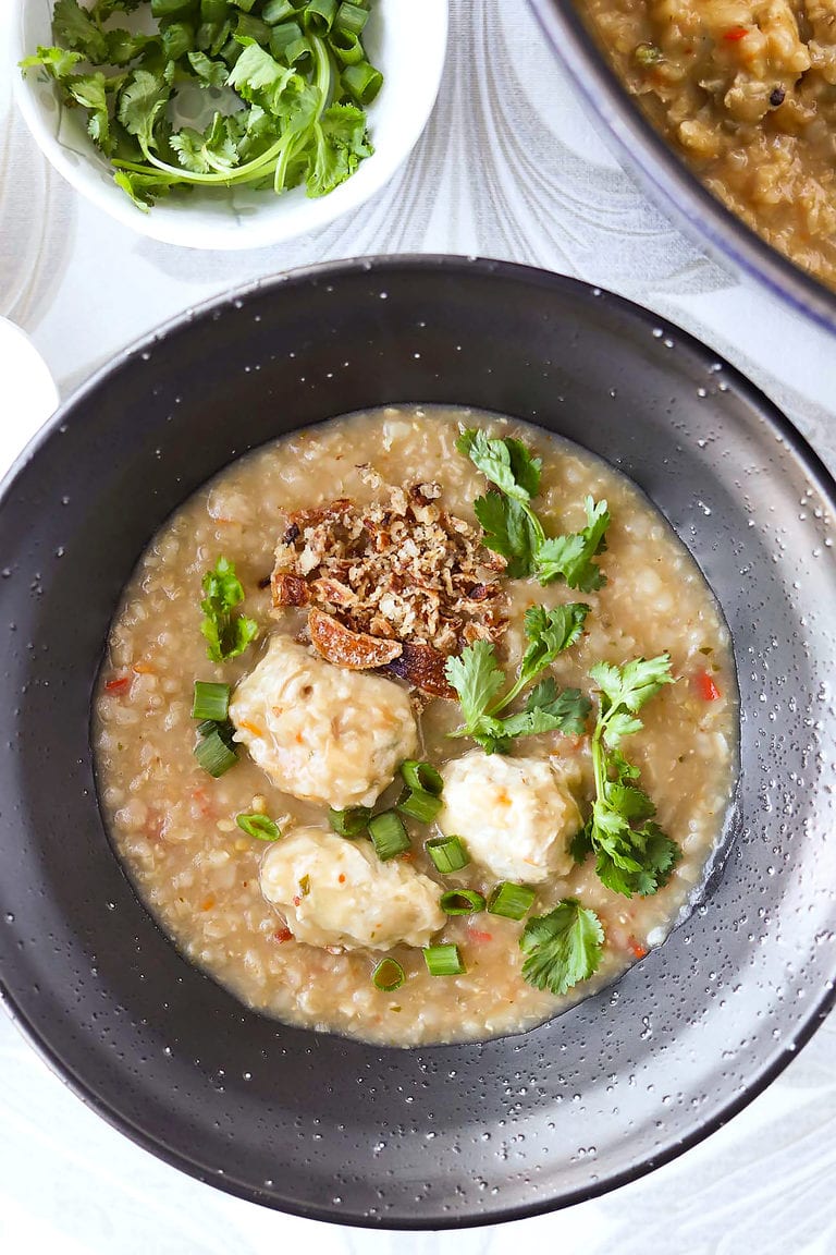 Thai congee with chicken meatballs topped with coriander, spring onion and fried shallots in a bowl.