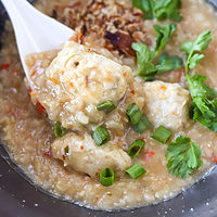 Spoon with a bite of congee and meatball closeup in a bowl. Text overlay "Thai Rice Porridge with Chicken Meatballs" and "thatspicychick.com".