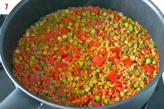 Cooked spiced rice in a skillet with onion, bell pepper and green peas.
