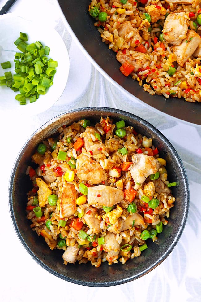 Bowl and wok with chicken fried rice. Small bowl with spring onion on the side.