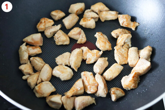 Cooking diced marinated chicken pieces in a wok.
