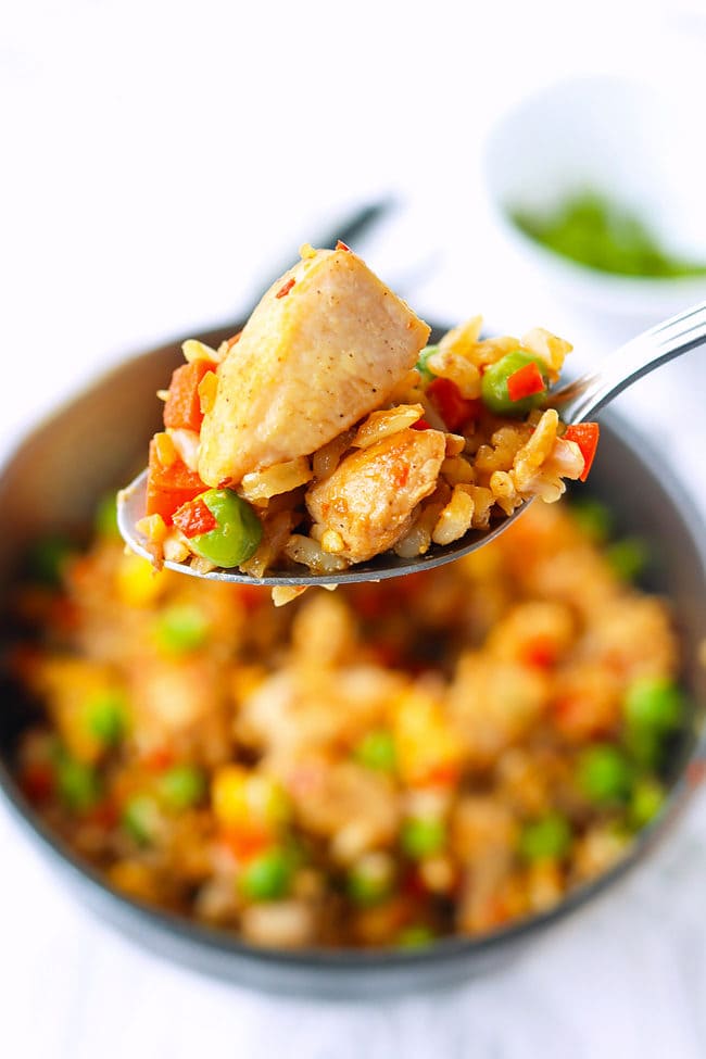 Spoon holding up a bite of chicken fried rice above a bowl.