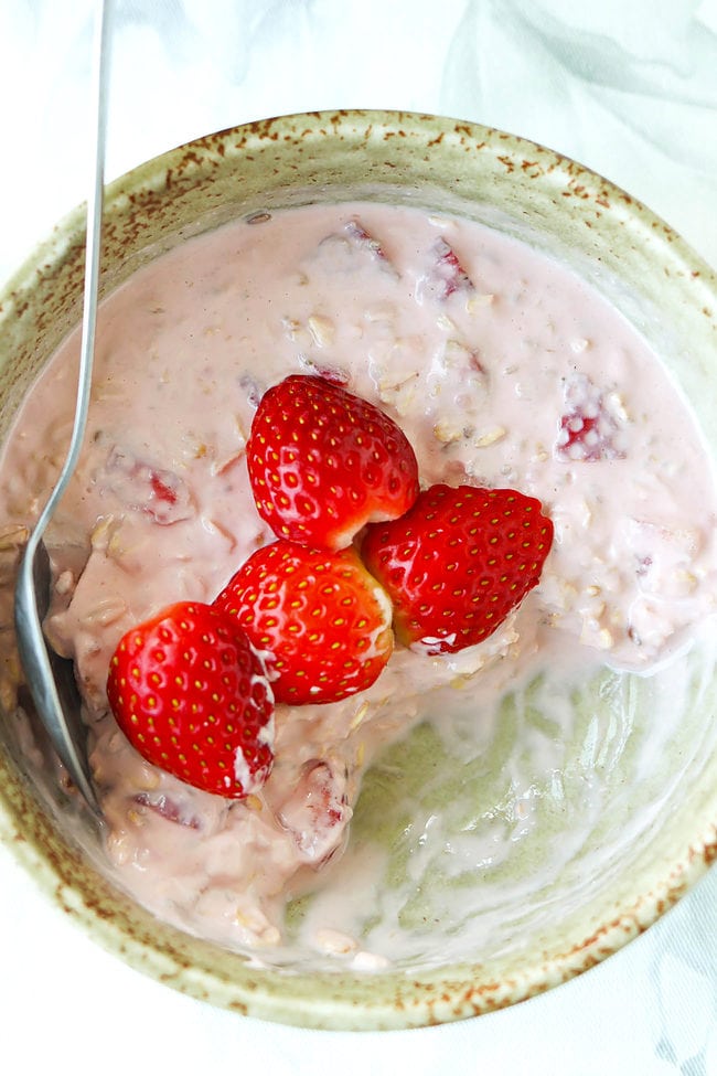 Bites eaten out of bowl with strawberry protein overnight oats topped with sliced strawberries and spoon.