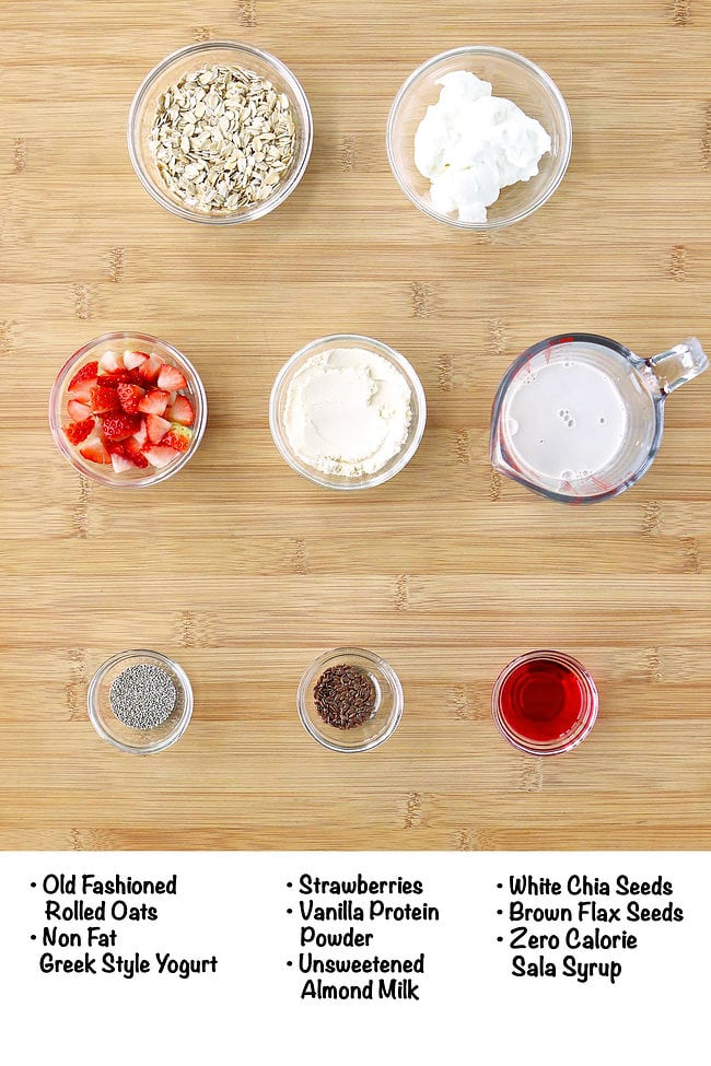 Labeled ingredients for strawberry protein overnight oats on a wooden board.