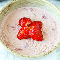 Bowl with pink overnight oats topped with fresh strawberries. Text overlay "Strawberry Protein Overnight Oats" and "thatspicychick.com".