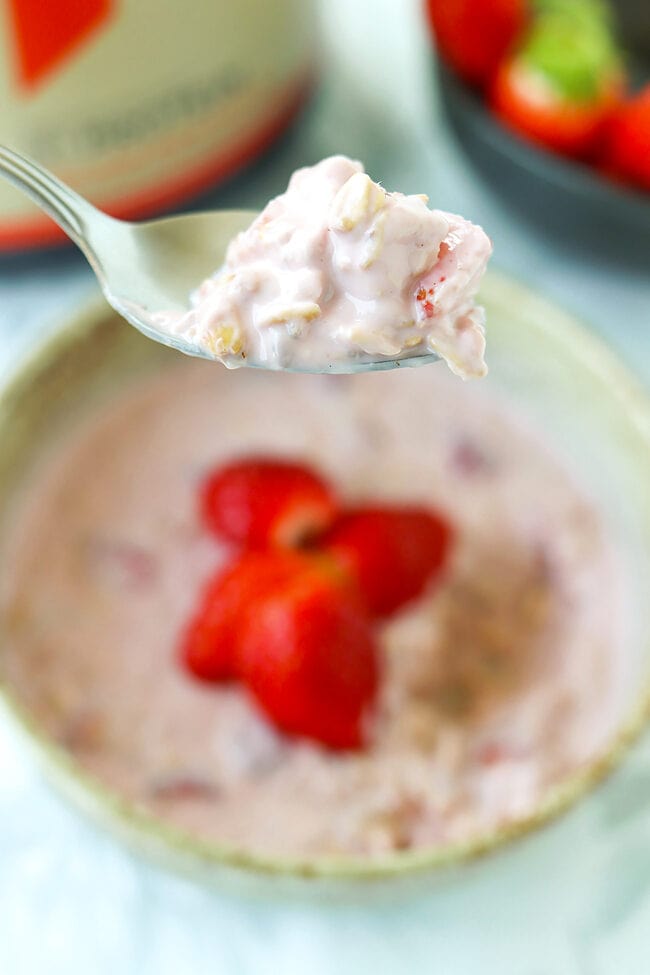 Spoon holding up a bite of strawberry protein overnight oats above a bowl.