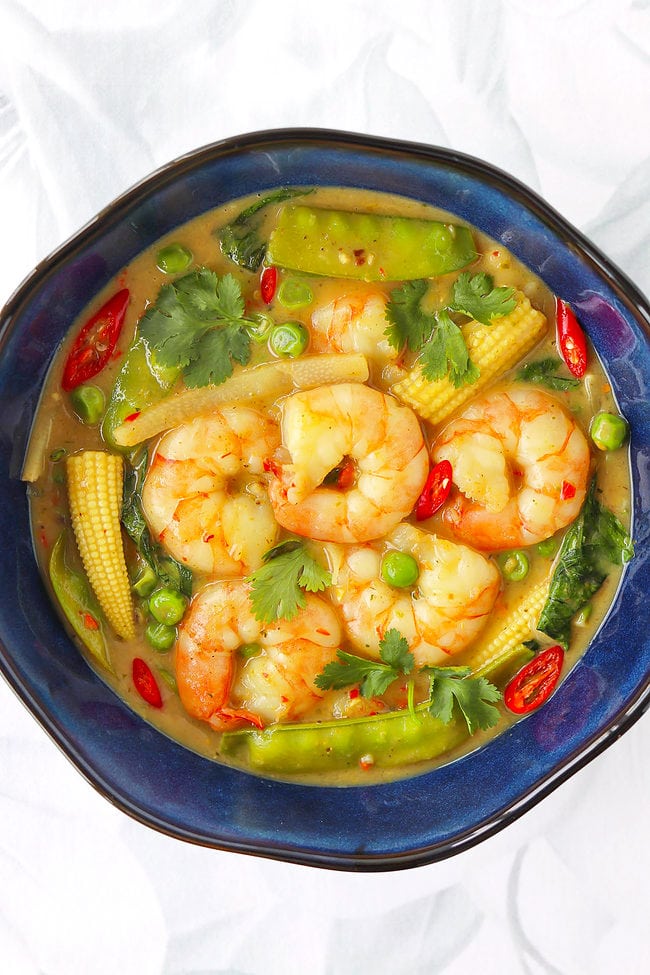 Overhead view of Thai green curry shrimp with vegetables in a blue bowl.