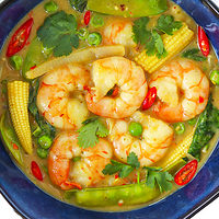Closeup overhead view of Thai green curry shrimp with vegetables in a blue bowl.