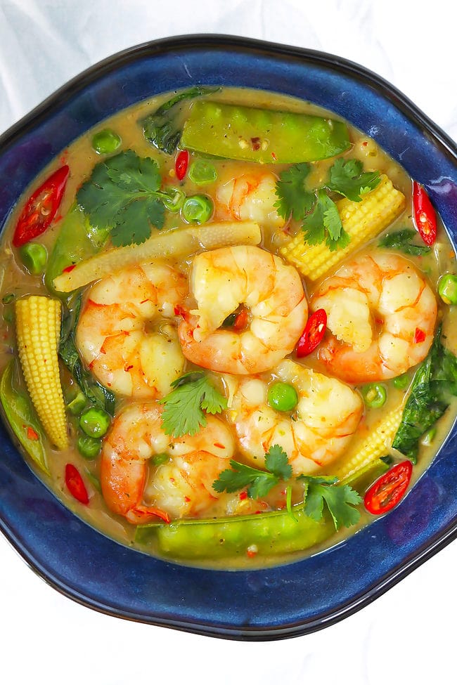 Closeup overhead view of Thai green curry shrimp with vegetables in a blue bowl.