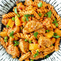 Close-up top view of peri peri pasta with chicken on a plate. Text overlay "High Protein Creamy Peri Peri Chicken Pasta" and "thatspicychick.com".