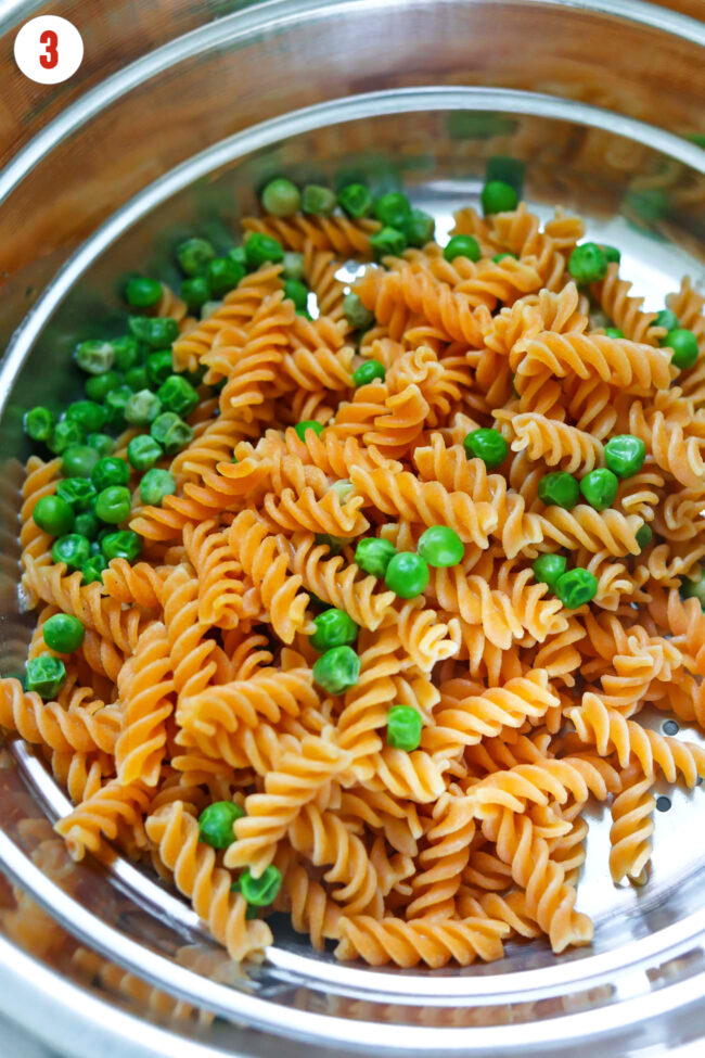 Cooked and drained red lentil fusilli and peas in a colander.