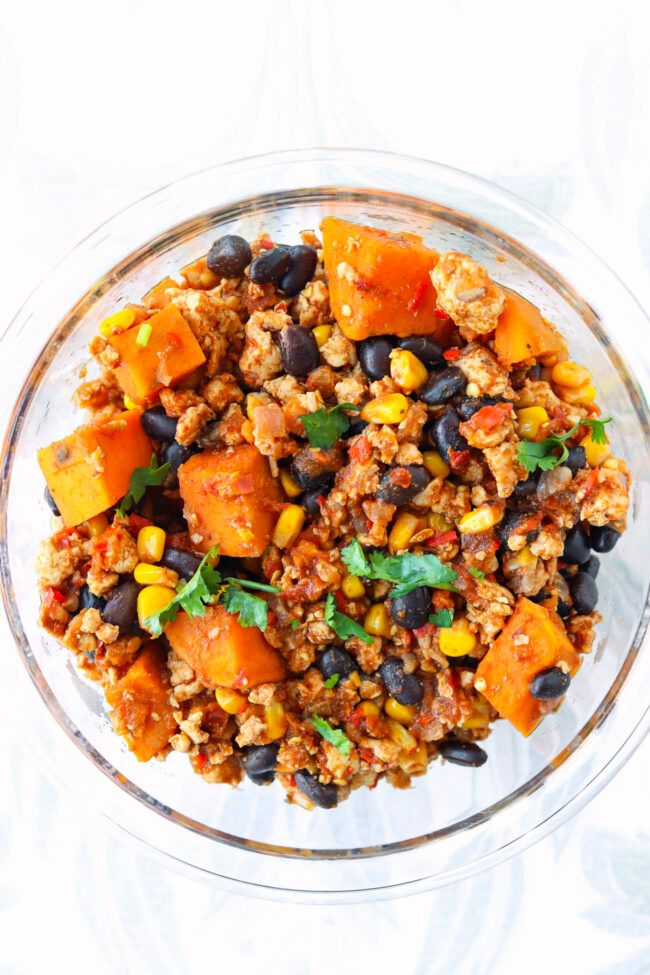 Ground chicken, sweet potato, black beans, corn garnished with coriander in meal prep container.